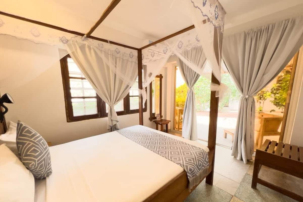 A bedroom with a bed, curtains, a bench, and a view of the outdoors.
