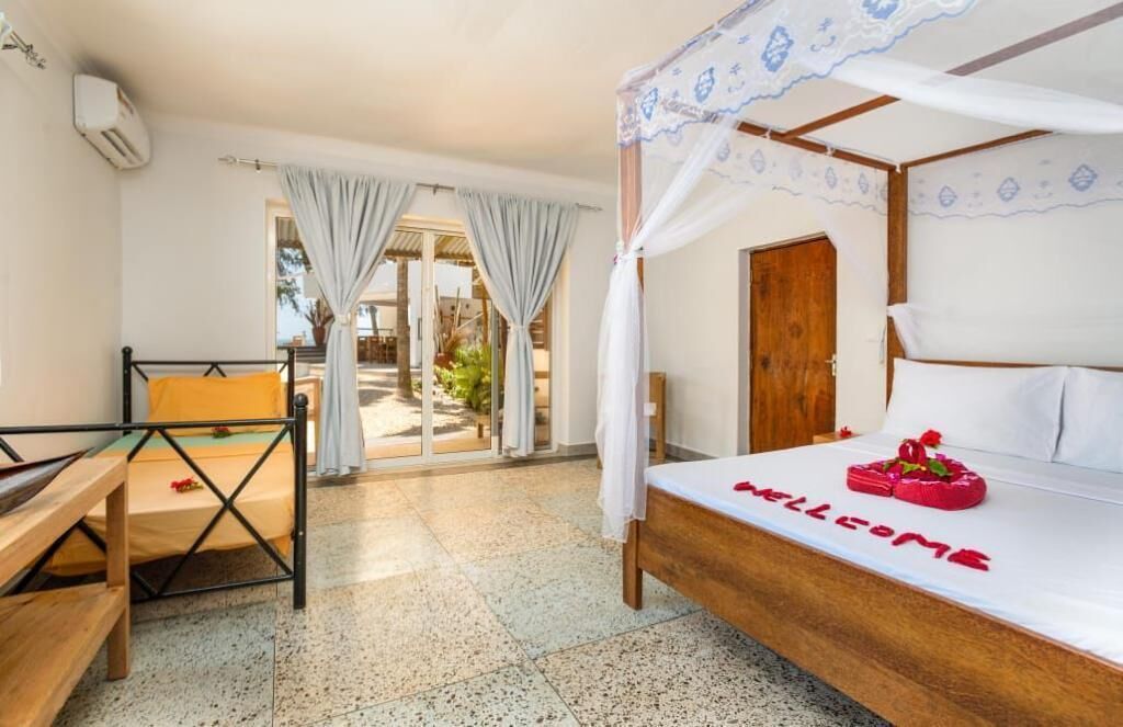 A bedroom with a bed, a bench, a door, and a view of the outside.