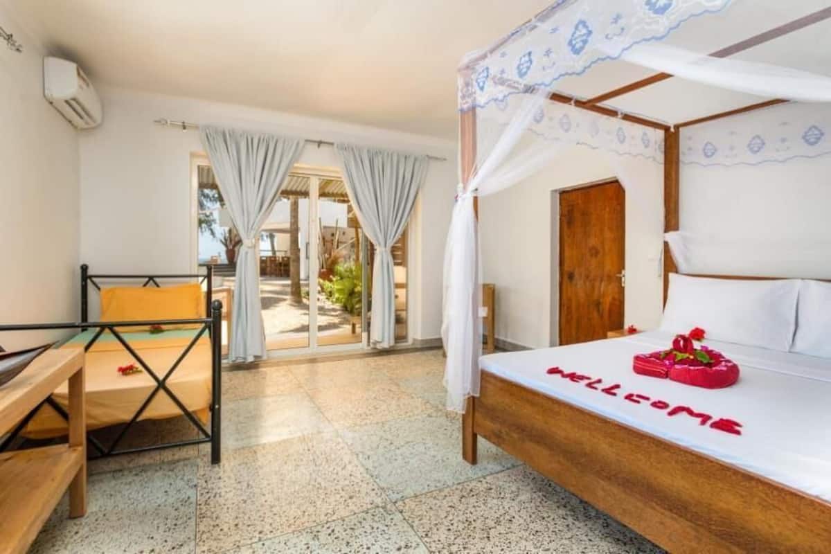 A bedroom with a bed, a bench, a door, and a view of the outside.