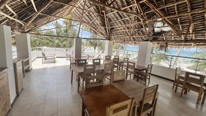 Un ristorante con mobili in legno e tetto di paglia, affacciato su una spiaggia.