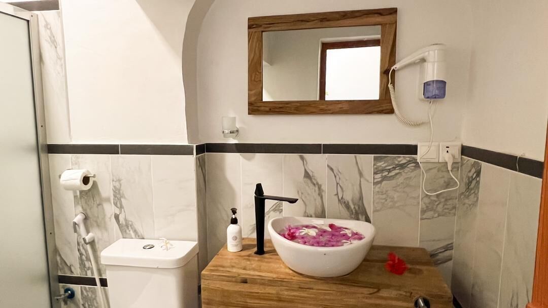 Ein Badezimmer mit Marmorfliesen, einem Holzkosmetikschrank, einem Waschbecken mit einer Blumen-Dekoration, einer Toilette und einer Duschkabine.