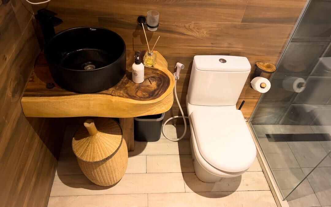 Une salle de bain moderne avec un meuble-lavabo en bois, un lavabo noir, des toilettes et une douche à parois de verre.