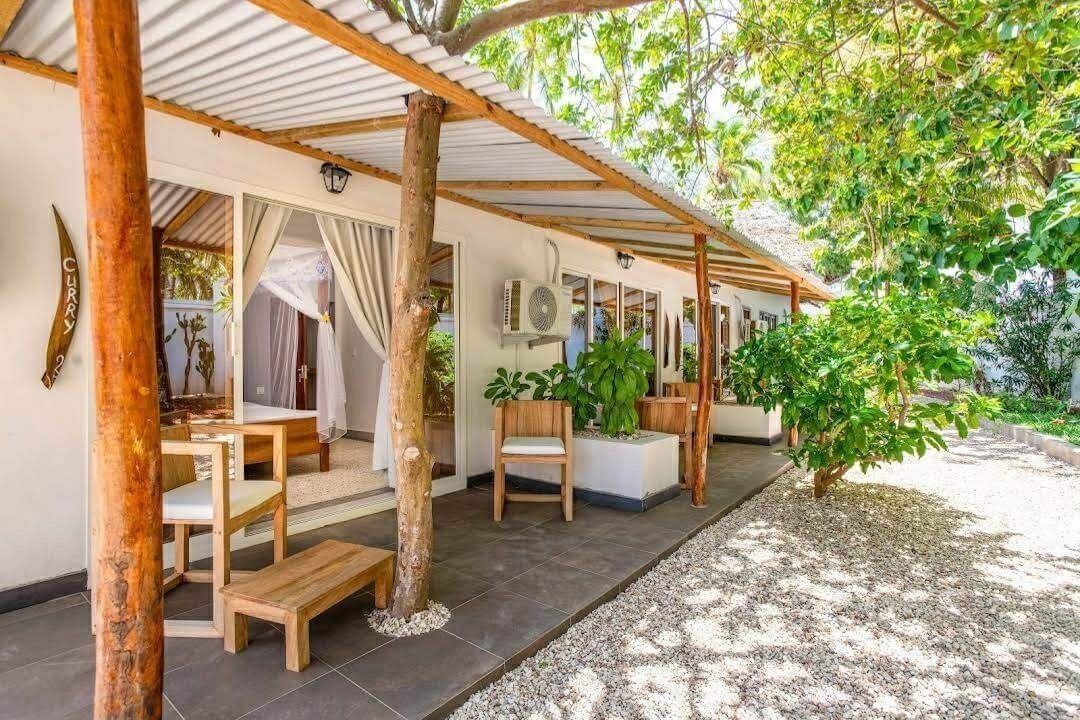 Un área de estar al aire libre techada con mobiliario de madera, una pérgola y plantas en macetas.