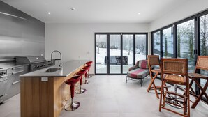 A modern kitchen with a central island, stainless steel appliances, and a large sliding glass door leading to a snowy outdoor area.