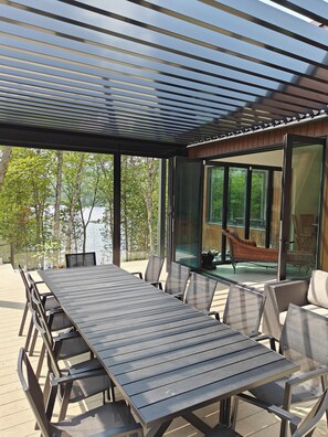 A covered outdoor dining area with a view of a lake and trees.