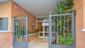 A brick building entrance with a metal gate, a sign reading "Edificio", and potted plants.
