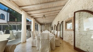 Un comedor amplio con manteles blancos y sillas, techo de madera y ventanas grandes.
