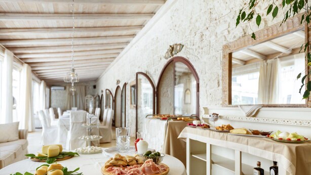 Un comedor con una mesa de buffet, sillas blancas y un espejo en la pared.