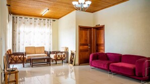 A spacious living room with a wooden ceiling, a red sofa, a beige sofa, wooden chairs, and a coffee table.