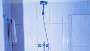 A bathroom with white tiles, a showerhead, and a towel rack.