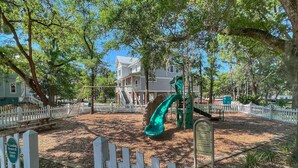 A playground with a green slide and climbing structures, surrounded by a white picket fence, with a building in the background. - Yellowfin in the Steinhatchee Landing (Steinhatchee)