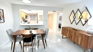 Een eetruimte met een marmeren vloer, een houten eettafel en grijs gestoffeerde stoelen. Tegen de muur staat een houten buffet, erboven hangt een grote spiegel.