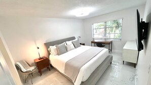 Een slaapkamer met een bed, nachtkastje, stoel, bureau en televisie.