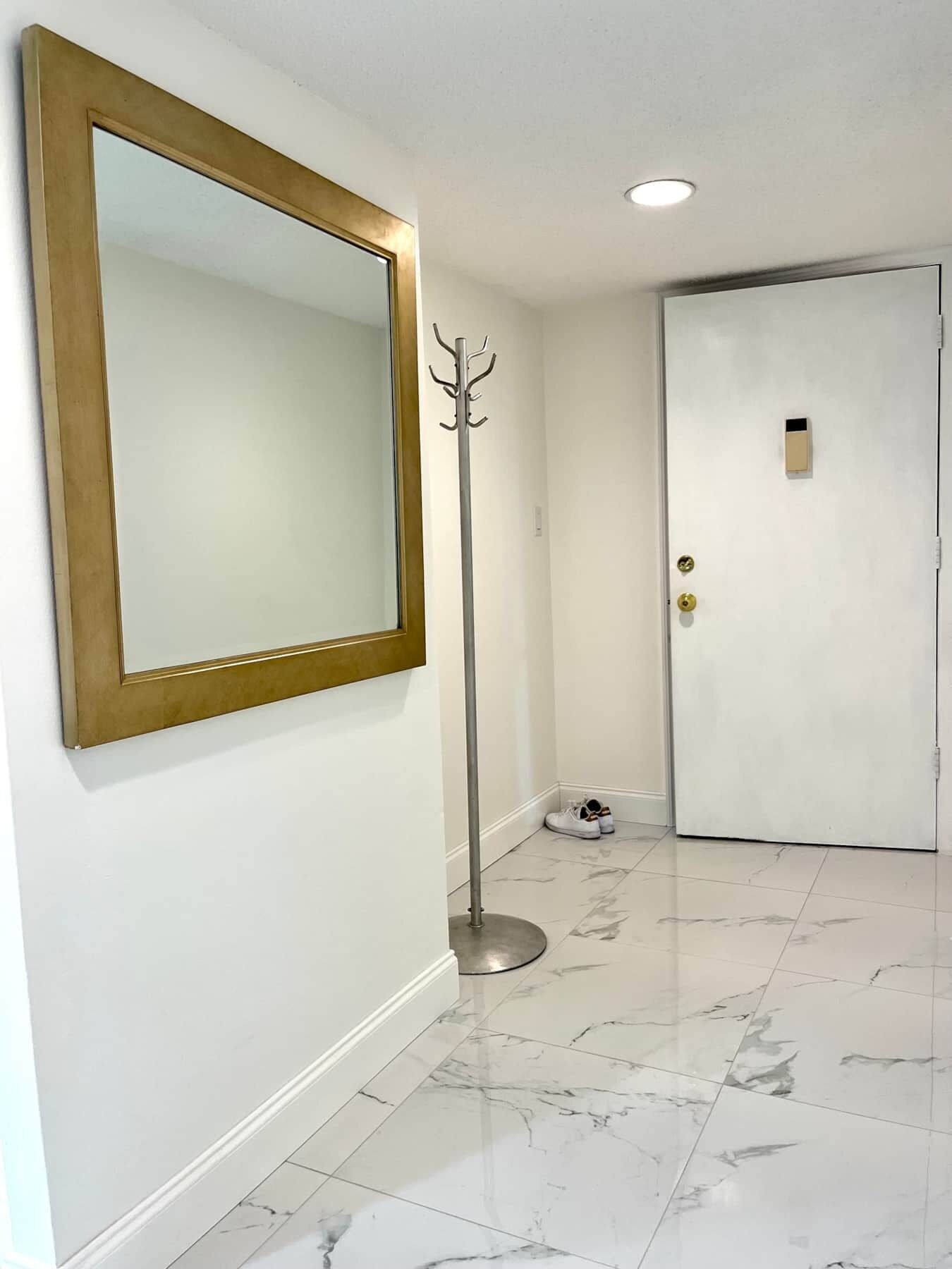 A hallway with a large mirror, a coat rack, and a door with a keycard lock.