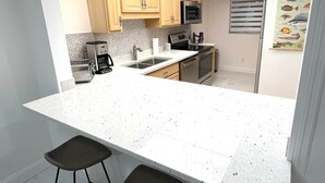 Een moderne keuken met een groot eiland, twee barkrukken, houten kastjes, roestvrijstalen apparatuur en een betegelde spatwand.