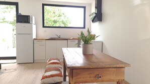 Eine Küche mit weißen Schränken, einem Holztisch, einem Blumentopf und einem Fenster mit Blick auf Grünflächen.