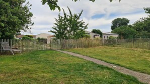 Ein Garten mit Rasen, einem Holzzaun, einem Kiesweg und einem Metallstuhl.