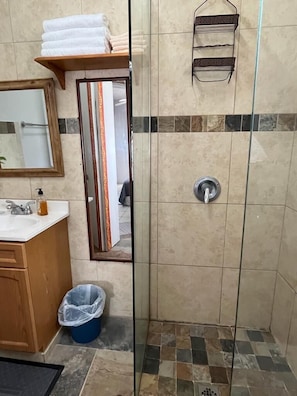 A bathroom with a shower, a sink, a mirror, and a towel rack.