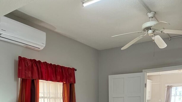 Un dormitorio con cama, mesita de noche, lámpara, ventilador de techo y ventana con cortinas.