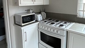 Una cocina con armarios blancos, microondas, tostadora y estufa a gas.