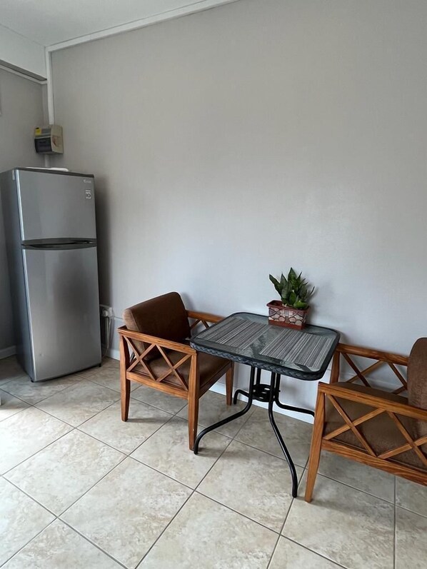 A compact living space with a kitchenette, including a refrigerator, a small table with chairs, and a potted plant.