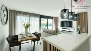 Eine moderne Küche mit Kochinsel, Essbereich mit Stühlen, einer großen Wanduhr und einem Fernseher im Hintergrund.