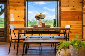 A wooden interior with a dining table, benches, and a window with a view of greenery. - Riverfront Retreat | Fish, Kayaking & Hot Tub (Broken Bow)