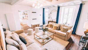 Een ruime woonkamer met een beigekleurige zithoek, een glazen salontafel en een houten vloer.