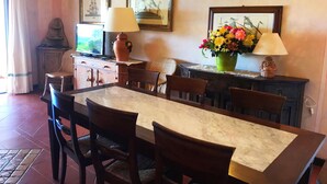 A dining area with a marble table, wooden chairs, a vase of flowers, and two wall-mounted lamps. - Cala del Faro - Maestrale (Arzachena)