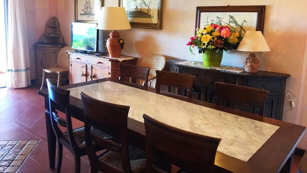 A dining area with a marble table, wooden chairs, a vase of flowers, and two wall-mounted lamps. - Cala del Faro - Maestrale (Arzachena)