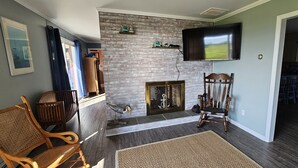 A living room with a brick fireplace, a mounted TV, and wooden furniture. - New Waterfront! Drop Anchor on Brannocks Bay. An Amazing waterfront retreat! (Cambridge)