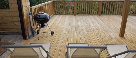 A wooden deck with a barbecue grill and two folding chairs.