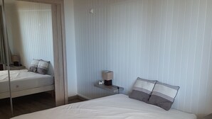 Een moderne slaapkamer met een groot bed, een nachtkastje met een lamp en een spiegel.