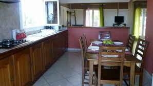 Een keuken met houten kastjes, een gasfornuis, een eettafel met stoelen en een raam met gordijnen.