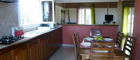 A kitchen with wooden cabinets, a gas stove, a dining table with chairs, and a window with curtains.