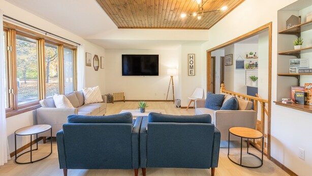 Uma sala de estar moderna com teto de madeira, uma TV grande e um espaço de estar aconchegante com sofás e uma mesa de centro.