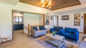 Uma sala de estar moderna com teto de madeira, um sofá cinzento, um sofá azul e uma pequena mesa com uma planta.