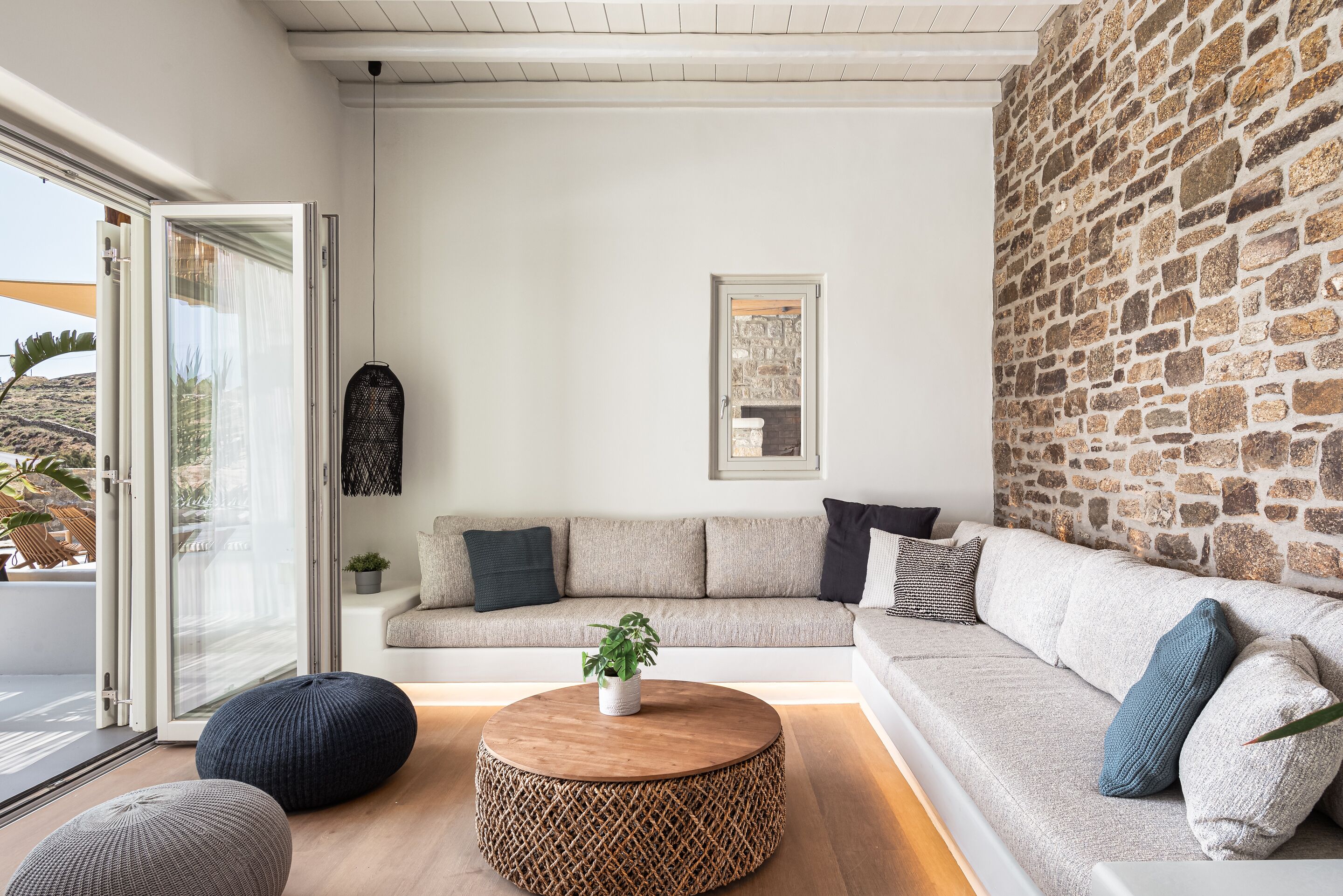 A modern living room with a stone wall, a sofa, a coffee table, and a large window.