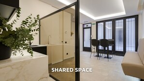 Ein moderner Gemeinschaftsbereich mit einer Marmorarbeitsplatte, einem Waschbecken, einer Topfpflanze, einer Sitzecke mit Stühlen und einem Sofa sowie einem großen Fenster mit Blick.