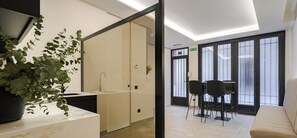 Un espacio compartido moderno con encimera de mármol, lavamanos, planta en maceta, zona de estar con sillas y sofá, y un ventanal con vistas.