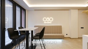 Ein modernes Interieur mit einer Couch, Sesseln, einem Tisch und einer Wand mit beleuchteter 'OSO MADRID'-Beschriftung.