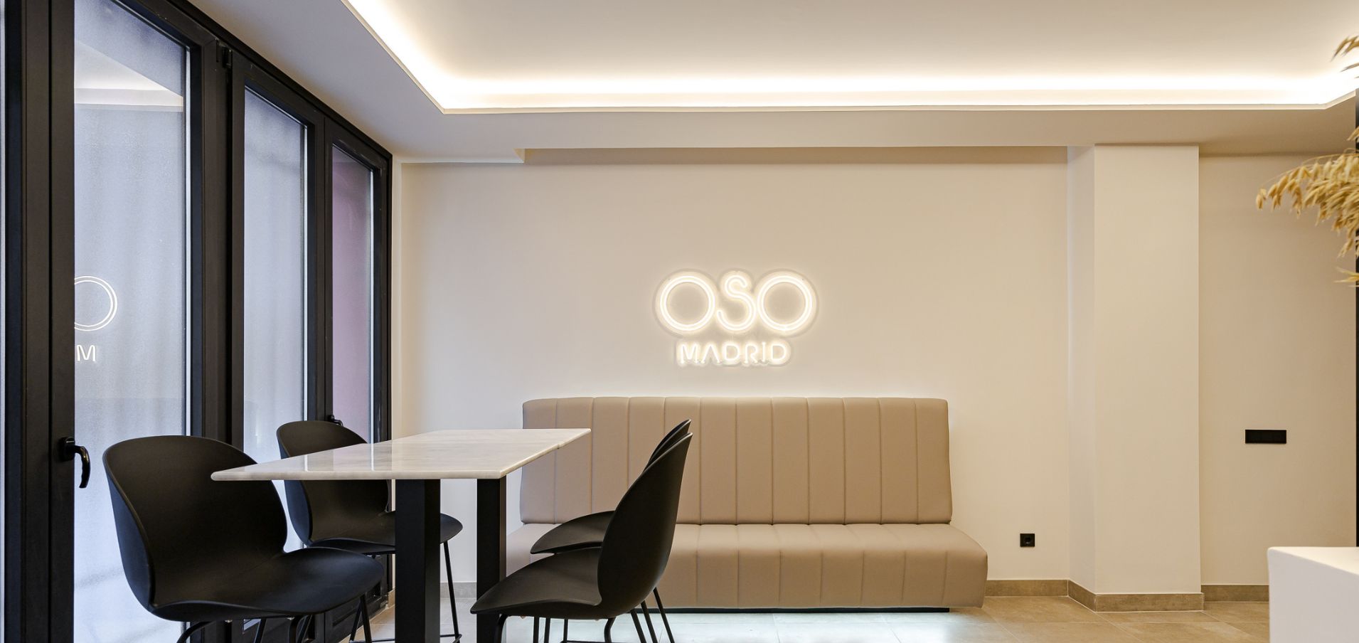 Moderni sisustus, jossa on sohva, tuoleja, pöytä ja seinä, jossa on valaistu kyltti, jossa lukee ”OSO MADRID”.