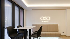 Un intérieur moderne avec un canapé, des fauteuils, une table et un mur orné d’une enseigne lumineuse portant l’inscription « OSO MADRID ».