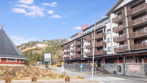 Un hôtel à plusieurs étages doté de balcons, avec une piste de ski en arrière-plan et un passage piéton.