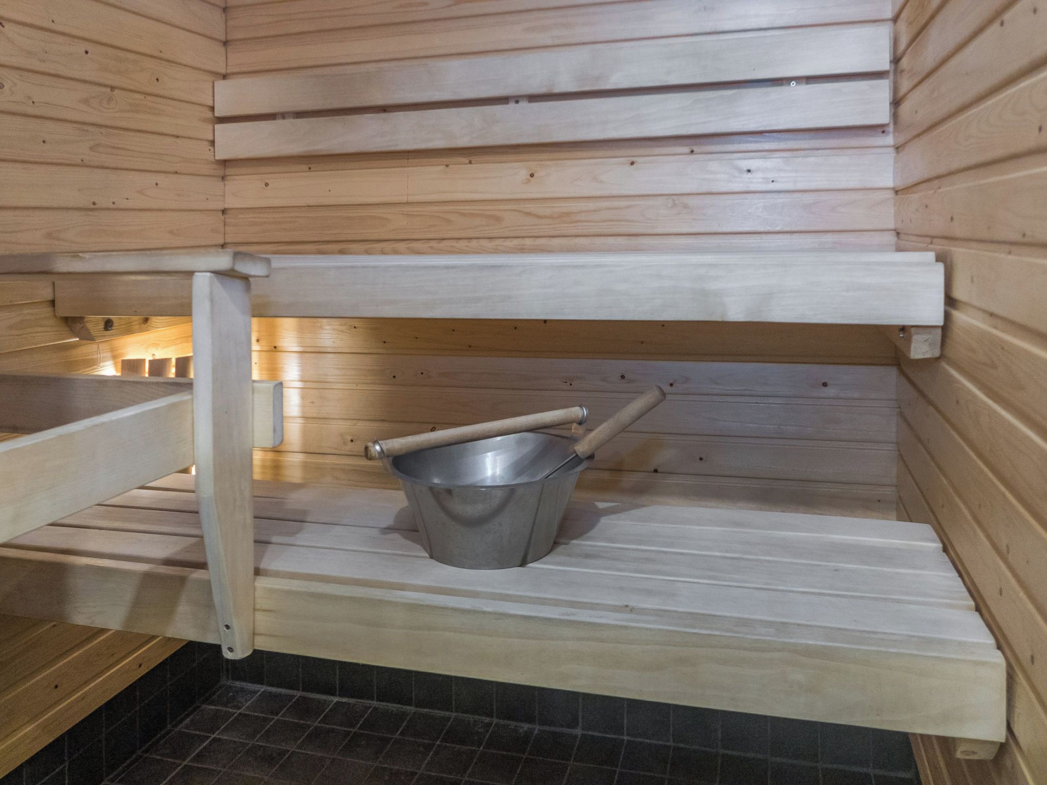 A sauna with wooden walls, a metal bucket, and a wooden bench.
