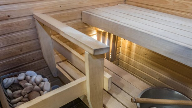 Un sauna avec des bancs en bois, un bassin en pierre et une louche en bois.