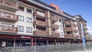 Un hôtel à plusieurs étages doté de balcons, une enseigne indiquant un chalet de ski, et un restaurant appelé « KOKSA ».