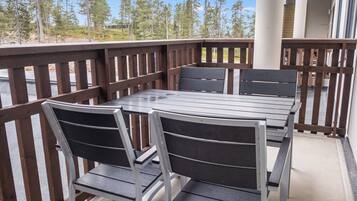 Terraza de madera con mesa y sillas, con vista a un área boscosa.