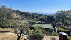 Un court de tennis entouré d’arbres et de collines, offrant une vue dégagée sur la mer.