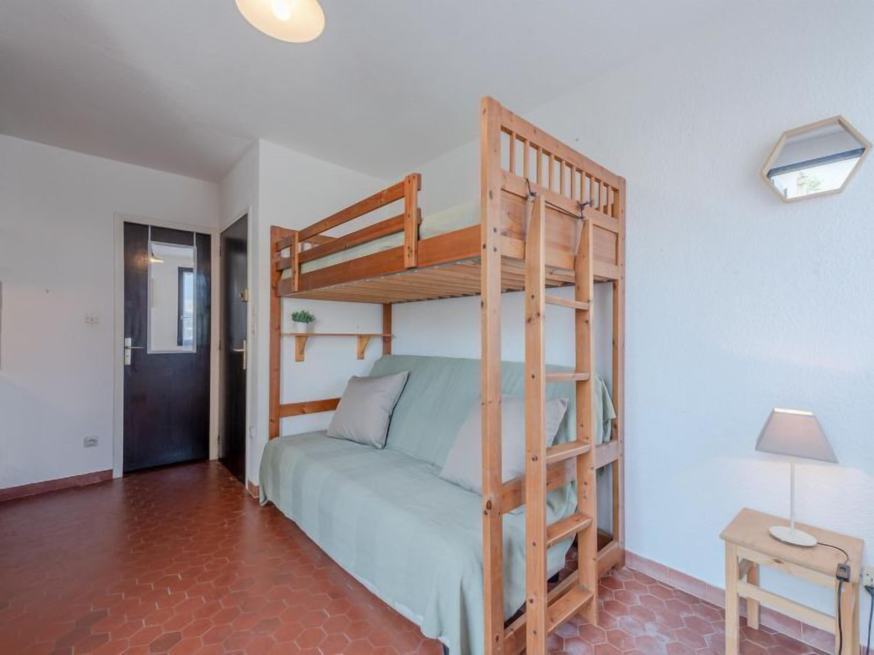 Une pièce avec un lit superposé, une petite table avec une lampe et une porte.